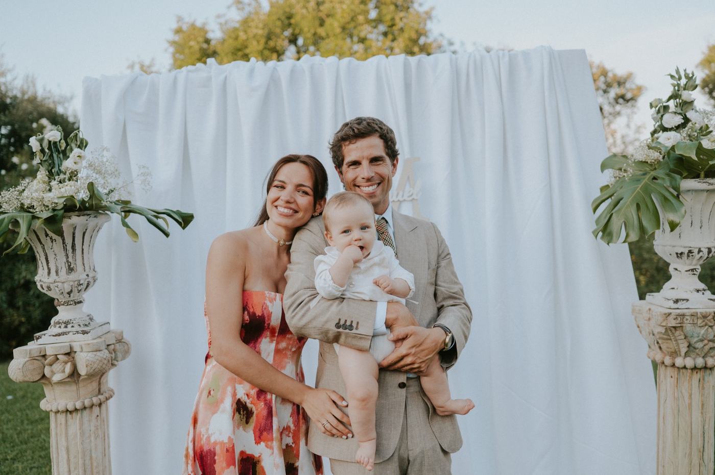 Pais com o bebé junto ao cenário branco no jardim