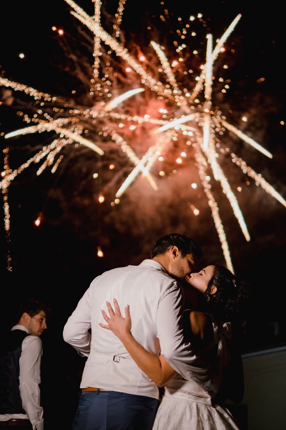 Beijo dos noivos sob o fogo de artifício
