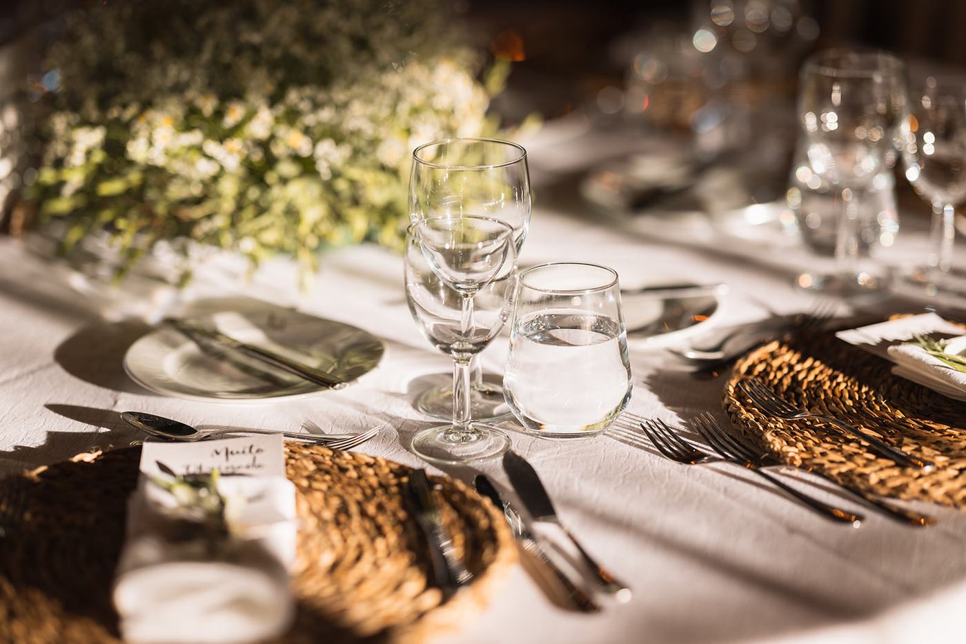 Mesa posta com copos de cristal e pratos de rattan